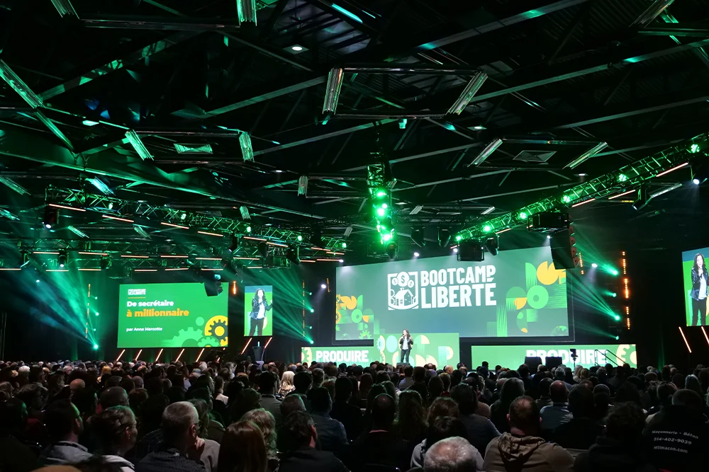 stage setup of Bootcamp Liberté of large LED screens with the logo, with a green light theme. The audience in the foreground.